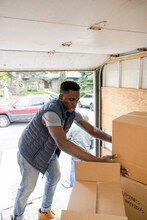 Male Mover Loading Cardboard Boxes Into Moving Van