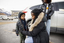 Mother Fastening Son's Coat Next To Car