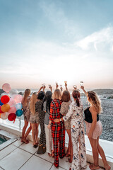 Warm and atmospheric portrait of a eight women rising their hands up holding glasses with champagne.