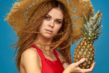 A woman in a straw hat with a pineapple in her hands or is it a fun blue exotic fruits background