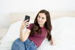 © lili - selfie. girl with a phone in her hands. girl looking at the phone lying on the bed at home