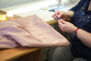 Wall Mural - Talented female seamstress working with textile for sewing clothes. Close up view of sewing process. Light blurred background