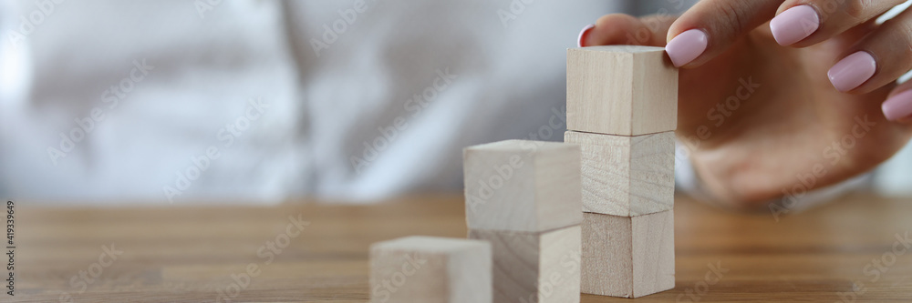 Female hand builds tower from wooden blocks. Successfully building a career in business for women concept - obrazy, fototapety, plakaty 