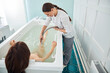 Friendly spa worker female massaging client right leg with water