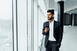 © Тарас Нагирняк - A serious bearded Indian man uses his modern phone, he is in a black suit in the middle of a modern building, an office worker, a boss, a manager
