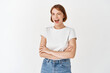 © Cookie Studio - Happy candid woman in t-shirt and jeans, winking and smiling at camera, motivating you, cross arms on chest and look joyful, standing on white background