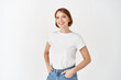© Cookie Studio - Cheerful natural girl in t-shirt and jeans smiling, looking upbeat, standing against white background