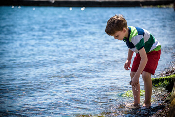 The little boy by the sea throws stones in water. Relaxation and vacation with kids. Happy childhood