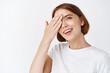 © Cookie Studio - Close up portrait of beautiful natural woman, covering eye and smiling at camera, showing skin care routine cosmetics, standing against white background