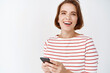 © Cookie Studio - Portrait of happy caucasian woman in striped blouse, laughing and smiling, chatting on smartphone and smiling, standing against white background