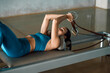 © BASILICOSTUDIO STOCK - Close up of upper body of a Woman lying down on a bed of a Pilates Reformer machine, pulling a stretch band with her arms, training in a Fitness Gym Studio.