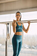 © BASILICOSTUDIO STOCK - Brunette fit woman taking a break after Pilates exercises on a Trapeze table, holding the bars of the machine. Young sporty woman looking aside during workout. In a big gym studio with wide windows.