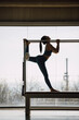© BASILICOSTUDIO STOCK - Full length shot of a female Pilates instructor realizing stretching routine, on a Cadillac Machine, Trapeze Table in a big Fitness Studio with wide windows and outside views. Backlight, silhouette.