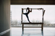 © BASILICOSTUDIO STOCK - Full shot of a big Fitness Gym with wide windows and street views, with a fit female Pilates instructor realizing stretching routine, on a Cadillac Machine, Trapeze Table. Backlight, silhouette.