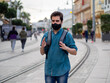 © David Martínez - Hombre joven con mochila caminando por la calle vistiendo una mascarilla negra cumpliendo las medidas de seguridad y distanciamiento social de la pandemia del coronavirus