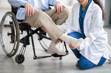 Wall Mural - Cropped view of young doctor checking disabled senior patient's leg during medical visit at home