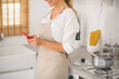 © zinkevych - Woman in apron standing in the kitchen with a tablet in hands