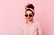© Look! - Close-up portrait of girl with red lips and bun in sunglasses. Woman in pink headband and cotton shirt is smiling on isolated background