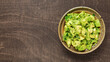 Bowl of freshly made chunky guacamole on brown wooden background with copy space for text.