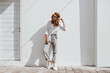 © Look! - Stylish girl in gray pants and white cotton blouse posing near white wall. Photo of woman in cap and glasses