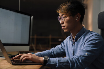 Sticker - Focused asian guy working with laptop while sitting at table in office