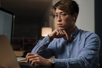 Sticker - Focused asian guy working with laptop while sitting at table in office