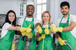 © sofiko14 - Smiling multiracial housekeepers in green apron and yellow gloves showing thumbs up at work. Happy professional cleaner team gesturing on camera at bright room.