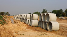 Round Concrete Sewer Piles On The Ground. Stacked Pipes For Sewer Systems In Road Construction Areas On Green Tree Background And Blue Sky With Copy Space. Selective Focus