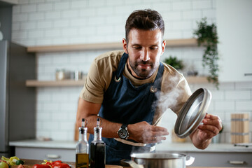 Wall Mural - Handsome man preparing pasta in the kitchen. Guy cooking a tasty meal..