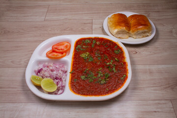 Wall Mural - Pav Bhaji is a fast food dish from India, thick and spicy vegetable curry, fried and served with a soft bread roll / bun paav and butter. Served on a colorful or wooden background. selective focus