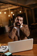 Wall Mural - Young businessman working with laptop at office. Tired man sitting at office desk working on laptop computer