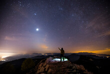 Rear View Of A Man Standing On A Mountain At Night Pointing To Sky, Mare De Deu Del Mont, La Garrotxa, Girona, Catalonia, Spain