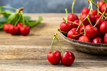 Ripe sweet cherries with green leaves in a metal plate on wooden background