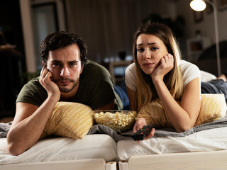 Wall Mural - Young loving couple relaxing on bed together. Happy couple watching movie at home.