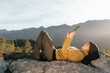 © Alberto Menendez/ADDICTIVE STOCK - Side view of content female traveler lying with cup of hot drink and reading interesting book on background of spectacular mountainous landscape on sunny day