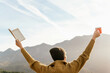 © Alberto Menendez/ADDICTIVE STOCK - Back view of unrecognizable female explorer standing with book and cup of hot drink in raised hands and enjoying freedom in mountains on sunny day