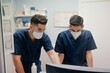 © Alberto Ortega/ADDICTIVE STOCK - Anonymous young male doctors in respiratory masks and uniforms working on desktop computer in clinic