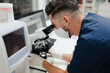© Alberto Ortega/ADDICTIVE STOCK - Side view of crop anonymous male medic in uniform and mask using microscope while working in lab