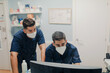 © Alberto Ortega/ADDICTIVE STOCK - Anonymous young male doctors in respiratory masks and uniforms working on desktop computer in clinic