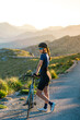 © Alvaro Imbert/ADDICTIVE STOCK - Full body of pensive female in sportswear with helmet standing with bicycle on empty roadway in majestic mountains