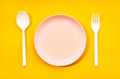 © Andres Victorero/ADDICTIVE STOCK - Top view composition with white plastic spoon and fork arranged near empty plate on yellow background