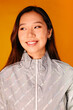 © Victor Torres/ADDICTIVE STOCK - Portrait of Asian young woman with serious expression. She wears a grey jacket and is looking away against a yellow background