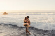 © Carlos Pintau/ADDICTIVE STOCK - Full length of cheerful young man carrying girlfriend and walking out of waving sea water while spending sunset time together on beach of Tenerife island