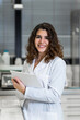 © Carlos Pintau/ADDICTIVE STOCK - Positive young female scientist in white coat with papers in hands smiling and looking at camera while working in modern medical lab