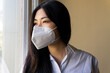© David Munoz/ADDICTIVE STOCK - Side view of young ethnic female executive in respiratory mask looking away against window in workspace