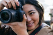 © David Munoz/ADDICTIVE STOCK - Ethnic young happy Asian female photographer shooting photo on professional photo camera on city street