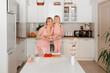 © Elena - Mom and daughter cook in the kitchen. A young woman cooks with her child in the kitchen at home. Girls in pink clothes cook pizza. Happy and cheerful mom and daughter