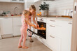 © Elena - Mom and daughter cook in the kitchen. A young woman cooks with her child in the kitchen at home. Girls in pink clothes cook pizza. Happy and cheerful mom and daughter