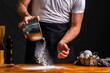 © Gaston Enria/ADDICTIVE STOCK - Faceless man in black apron dusting wooden table with wheat flour making bread in bakery