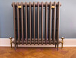Old fashioned cast iron radiator with brass fittings on herringbone wooden floor